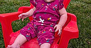 Aria is registered to the contest to win money with this photo: baby, casual_clothing, child, cute, daylight, floral_pattern, grass, greenery, infant, lawn, nature, outdoor, person, plastic_chair, purple_outfit, red_chair, serious_expression, sitting, summer, young_child