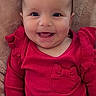 baby, smiling, red_clothing, infant, face, happy, cushion, blanket, indoor, child, portrait, cute, seated, young_child, apparel, warm, cozy, babysitter, joy, expression