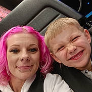 Hendrix is registered to the contest to win money with this photo: woman, child, selfie, pink_hair, smile, happy, seat, ride, amusement_park, straps, casual_clothing, hoodie, boy, portrait, fun, indoor, neon_lights, entertainment, face, people