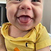 Carson is registered to the contest to win money with this photo: baby, child, tongue, smile, yellow_shirt, close_up, happy, face, skin, person, infant, cute, expression, indoors, human, young, joyful, portrait, sleeve, hand