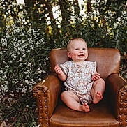Montana is registered to the contest to win money with this photo: baby, child, smiling, armchair, leather, flower, nature, outdoor, greenery, plant, portrait, happy, cute, infant, sitting, sunlight, face, skin, clothing, grass