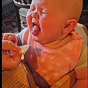 Gracie-May joined the competition — help win amazing prizes! baby, child, high_chair, pink_bib, polka_dot, tongue_out, lemon_slice, hand, wooden_table, wooden_chair, indoor, funny_face, expression, cute, dining_room, person, close_up, infant, feeding_time, reaction