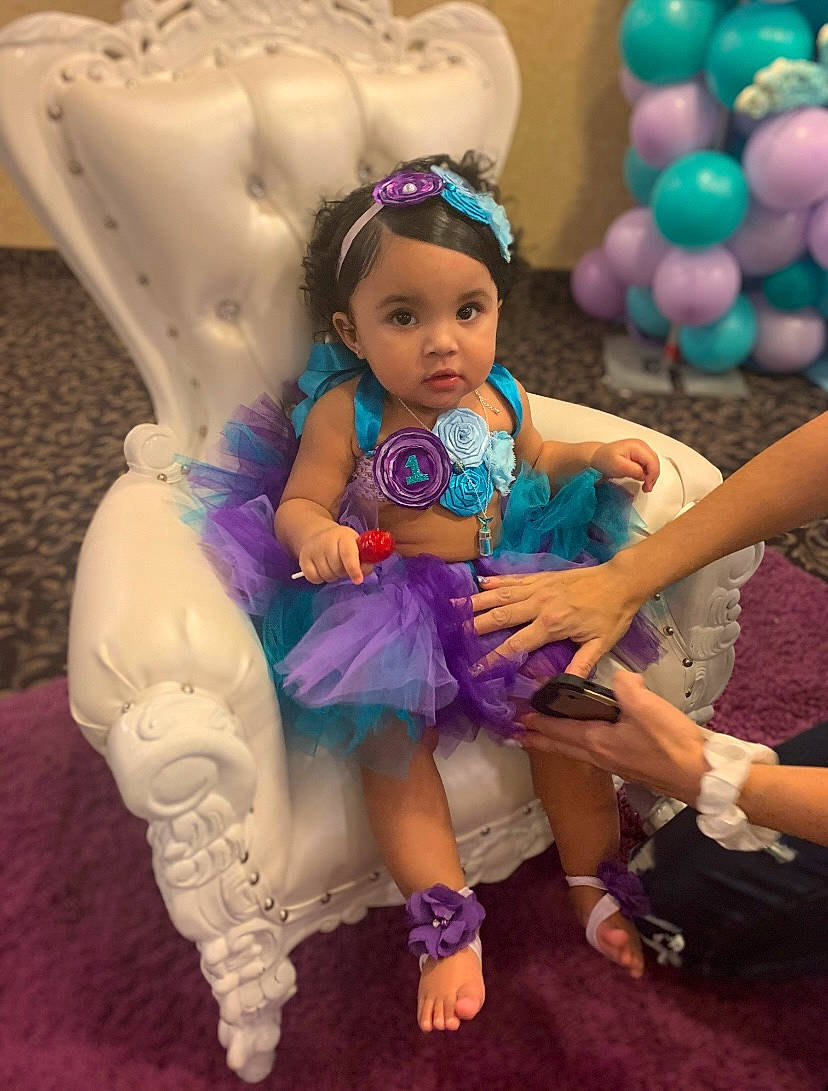 Lavanise is registered to the contest to win money with this photo: arm, balloon, chair, child, doll, dress, event, fun, hand, happy, headpiece, leisure, magenta, party_supply, person, pink, purple, recreation, sitting, toddler