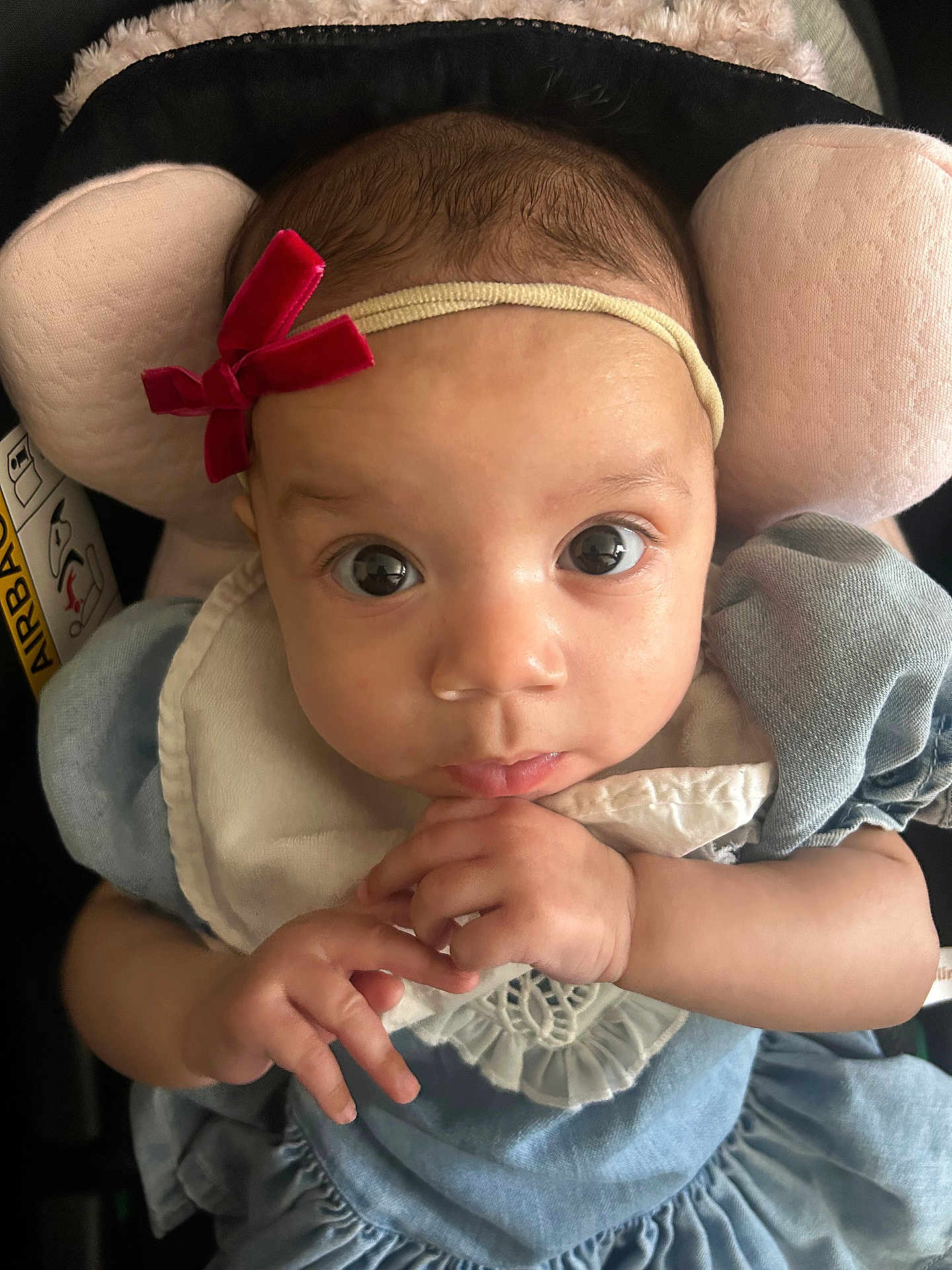 Amiyah is registered to the contest to win money with this photo: baby, infant, headband, bow, blue_dress, hands, face, eyes, curious, soft_cushion, pink, car_seat, clothing, portrait, closeup, child, cute, indoors, person, young