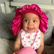 Amiyah joined the competition — help win amazing prizes! baby, pink_bonnet, bib, balloon, butterfly_pattern, smiling, sitting, blanket, cozy, infant, cute, happy, indoors, child, portrait, playful, hand, foot, headwear, expression