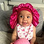 baby, pink_bonnet, bib, balloon, butterfly_pattern, smiling, sitting, blanket, cozy, infant, cute, happy, indoors, child, portrait, playful, hand, foot, headwear, expression