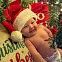 baby, santa_hat, christmas, holiday, infant, smile, pillow, diaper, christmas_tree, greenery, lights, festive, cute, indoors, cheerful, seasonal, happy, holiday_decor, child, portrait