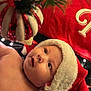 baby, infant, santa_hat, christmas, ornament, holiday, festive, decoration, closeup, face, cheeks, curious, soft_lighting, red, white, green, background, seasonal, warm, cute