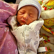 Atlas is registered to the contest to win money with this photo: newborn, baby, sleeping, infant, portrait, beanie, hat, onesie, dinosaur_print, swaddled, blanket, bedding, cushion, indoors, nursery, peaceful, closed_eyes, face, child, cozy