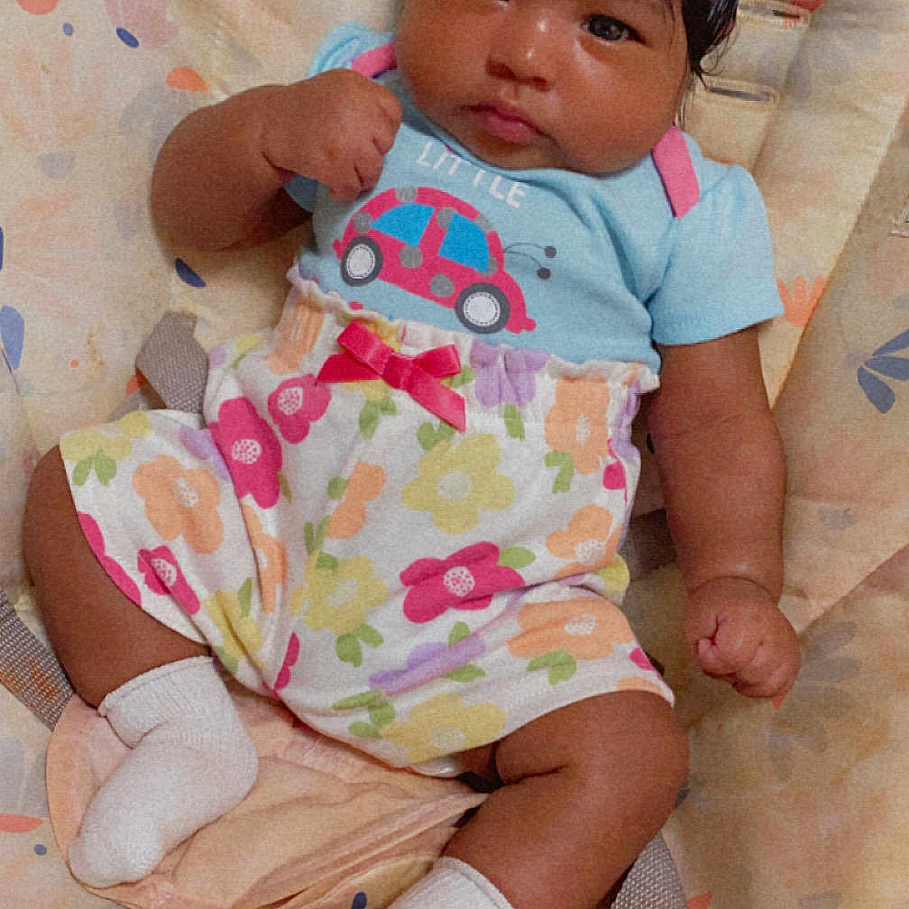 Karliynn is registered to the contest to win money with this photo: baby, child, clothing, colorful, cushion, cute, face, fist, floral, hair, indoor, infant, outfit, pattern, person, portrait, seat, sitting, socks, young