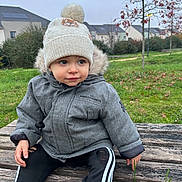 Sacha a rejoint le concours — aidez-le/la à gagner de superbes lots ! toddler, child, hat, pom_pom, jacket, outdoor, bench, grass, tree, autumn, leaves, overcast, park, curious, cold_weather, clothing, casual, person, nature, daytime