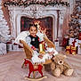 toddler, child, smiling, chair, gift, fireplace, christmas_decorations, wreath, christmas_tree, present, toy, teddy_bear, rocking_horse, holiday, indoor, flooring, cozy, festive, winter, celebration