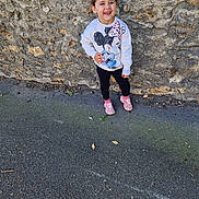 Kïarah a rejoint le concours — aidez-le/la à gagner de superbes lots ! child, smiling, standing, outdoor, stone_wall, sweatshirt, mickey_mouse, minnie_mouse, pink_shoes, casual_clothing, young_girl, happy, sidewalk, playful, fashion, daylight, person, cute, joyful, urban
