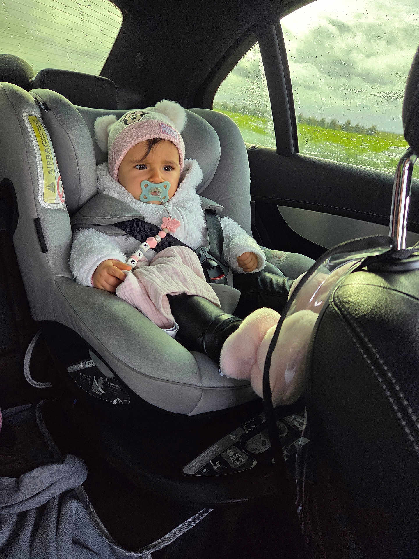 Lëynah a rejoint le concours — aidez-le/la à gagner de superbes lots ! baby, car_seat, pacifier, hat, winter_clothing, car_interior, window, rain, cloudy_sky, seatbelt, child, pink, black_boots, plush, person, infant, safety, transportation, cute, indoors