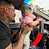 Jennifer is registered to the contest to win money with this photo: baby, man, tattoo, glasses, car_interior, steering_wheel, headband, bow, child, holding, driving, seat, window, clothing, person, adult, infant, hand, face, vehicle
