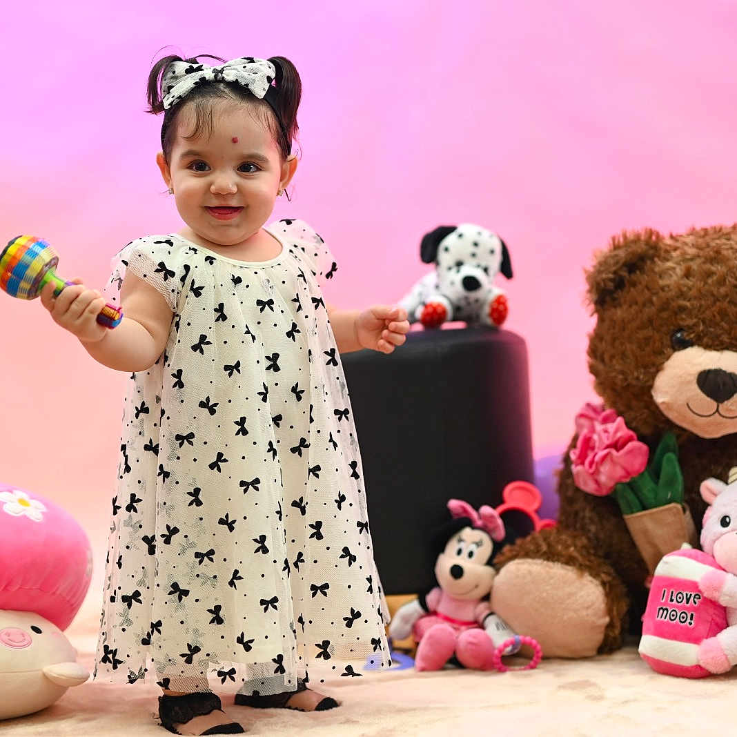 Allison joined the competition — help win amazing prizes! toddler, girl, child, dress, rattle, plush_toy, teddy_bear, mushroom_pillow, pink_background, bow, smile, toy_cow, toy_dog, toy_mouse, floor, indoor, cute, happy, playful, colorful