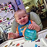 baby, bib, child, cute, drinkware, expression, face, food, furniture, high_chair, home, indoor, infant, kitchen, magnet, person, sippy_cup, smiling, sticker, table