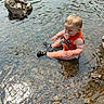 baby, barefoot, child, cute, exploring, happy, nature, orange_shirt, outdoor, pacifier, playful, river, rocks, shallow_water, sitting, splashing, summer, sunlight, toddler, water