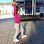 child, kid, person, side_view, profile, braids, pink_sweatshirt, patterned_pants, sneakers, playful, jumping, outdoor, paved_ground, urban, bench, information_board, signage, sunlight, shadow, smile