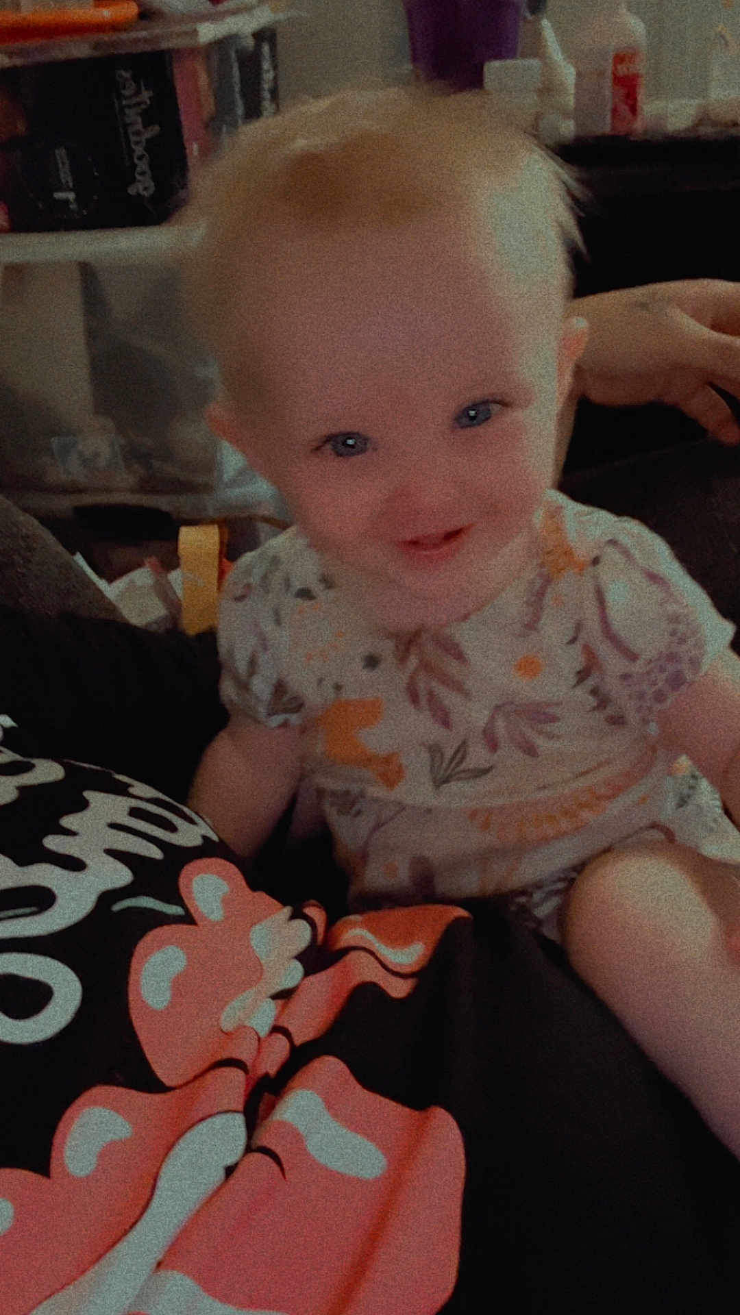 Alice is registered to the contest to win money with this photo: baby, child, smiling, portrait, indoor, person, clothing, floral_pattern, cute, happy, blue_eyes, sitting, short_hair, infant, colorful_shirt, cartoon_character, hand, cozy, casual, home