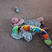 William is registered to the contest to win money with this photo: baby, baby_girl_or_boy, blanket, bottle, car_seat, carpet, carpet_texture, caterpillar_toy, child, clothing, colorful, cute, floor, indoor, infant, lying, person, playtime, small, toy