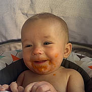Carson is registered to the contest to win money with this photo: baby, child, face, food, messy, smile, happy, infant, patterned_blanket, colorful, sitting, indoors, closeup, cute, skin, young_child, expression, mouth, hands, highchair