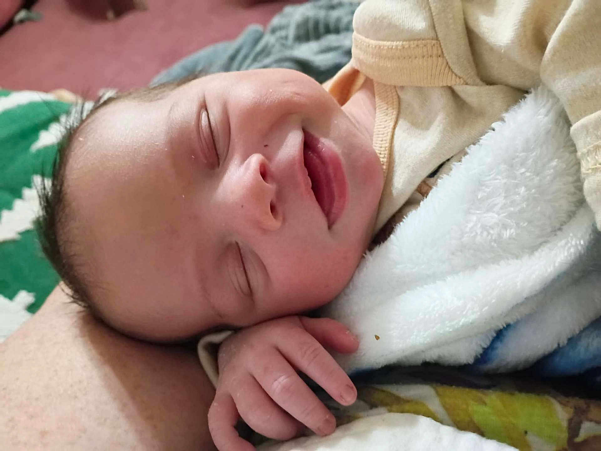 Oliver is registered to the contest to win money with this photo: baby, smiling, sleeping, blanket, hand, face, infant, clothing, cozy, comfort, closeup, skin, peaceful, child, portrait, cute, soft, indoors, newborn, resting