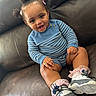 toddler, child, smiling, sitting, couch, leather, blue_sweater, striped_clothing, sneakers, pink_socks, hair_buns, hair_clips, happy, indoors, cute, portrait, baby, person, fashion, casual_wear
