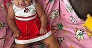 Germany is registered to the contest to win money with this photo: accessories, baby, cheerleader_outfit, child, couch, cute, flamingo_pattern, hair_buns, happy, indoor, infant, palm_tree_pattern, pink_blanket, playful, portrait, red_dress, sitting, smiling, socks, white_shoes