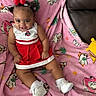 Germany is registered to the contest to win money with this photo: baby, child, smiling, cheerleader_outfit, red_dress, white_shoes, pink_blanket, flamingo_pattern, palm_tree_pattern, socks, cute, sitting, indoor, happy, infant, hair_buns, accessories, playful, couch, portrait
