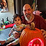baby, man, pumpkin, carved_pumpkin, glowing, portrait, indoor, pajamas, beard, smile, table, curtain, wall_art, face, child, adult, hand, light, decoration, family