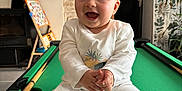 Côme participe au concours pour gagner de l'argent avec cette photo : baby, child, smiling, white_clothing, onesie, pool_table, green_felt, indoor, stone_wall, plant, wooden_cue, furniture, room, joyful, clapping, happy, portrait, infant, sitting, playful