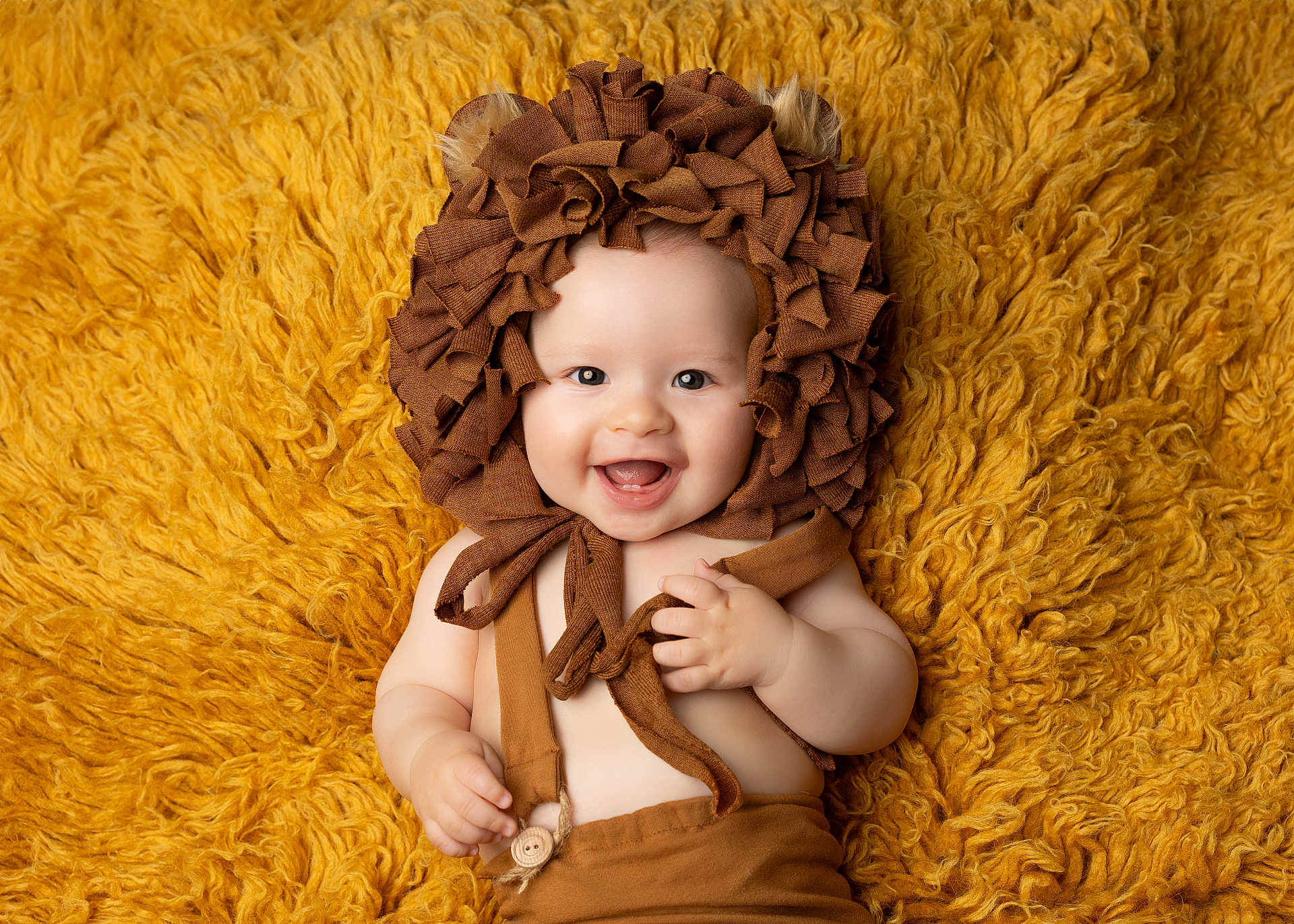 Côme participe au concours pour gagner de l'argent avec cette photo : baby, infant, smile, happy, face, portrait, costume, lion, bonnet, ears, cute, child, soft_texture, yellow, brown, fabric, clothing, lying_down, hands, closeup
