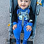 baby, child, stroller, smile, blue_clothing, nike, shoes, outdoor, pavement, seatbelt, happy, person, casual, cute, toddler, footwear, jumpsuit, toy, hand, face