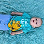 baby, baby_boy, blue_shirt, cartoon, casual, child, clothing, cute, green_blanket, happy_expression, infant, light_blue_pants, lion_king, lying_down, outdoor, patterned_blanket, portrait, relaxed, small_hands, soft_texture