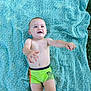 baby, bare_chest, blanket, child, cute, grass, green, happy, infant, lying_down, nature, outdoor, pattern, person, playful, shorts, skin, smiling, summer, young