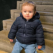 Elijah a rejoint le concours — aidez-le/la à gagner de superbes lots ! blue_pants, casual_clothing, child, clothing, cold_weather, concrete, curious_expression, daylight, jacket, outdoor, person, portrait, puffy_jacket, sitting, stairs, toddler, urban, wearing, young_boy, young_child