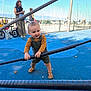 toddler, child, playground, rope, blue_surface, sandals, outdoor, daylight, woman, marina, boats, fence, people, casual, autumn_leaves, sky, urban, activity, fun, play