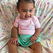 Evayah is registered to the contest to win money with this photo: baby, child, smiling, curly_hair, bow, pink_shirt, green_skirt, sitting, blanket, floral_pattern, indoors, cute, happy, portrait, toddler, skin, hand, foot, face, person