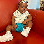Waliyya is registered to the contest to win money with this photo: baby, child, girl, headband, bow, white_tshirt, blue_shorts, white_socks, white_sneakers, orange_couch, indoor, furniture, cute, portrait, sitting, expression, skin, clothing, footwear, headwear