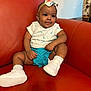 baby, child, girl, headband, bow, white_tshirt, blue_shorts, white_socks, white_sneakers, orange_couch, indoor, furniture, cute, portrait, sitting, expression, skin, clothing, footwear, headwear