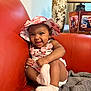 baby, child, smiling, hat, pink_socks, red_couch, blanket, indoor, decor, vase, picture_frames, happy, cute, portrait, toddler, clothing, sitting, person, infant, home