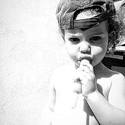 Jaron a rejoint le concours — aidez-le/la à gagner de superbes lots ! toddler, child, popsicle, hat, cap, curly_hair, outdoor, sunlight, shadow, diaper, bare_chest, wall, texture, summer, food, snack, portrait, person, young_child, playful