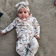 Mari is registered to the contest to win money with this photo: baby, carpet, casual, child, comfort, cute, floor, floral_clothing, headwrap, indoor, infant, lying_down, one_piece_outfit, patterned_clothing, person, portrait, small_feet, small_hand, soft_lighting, young_child