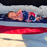 Kiara joined the competition — help win amazing prizes! baby, newborn, infant, flag, american_flag, stars, stripes, clothing, pattern, fabric, blanket, bed, lying_down, portrait, face, skin, hand, foot, indoors, soft_light