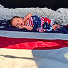baby, newborn, infant, flag, american_flag, stars, stripes, clothing, pattern, fabric, blanket, bed, lying_down, portrait, face, skin, hand, foot, indoors, soft_light