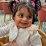 Enayah is registered to the contest to win money with this photo: background, cardigan, chair, child, dress, earrings, family, floor_tiles, happy, high_chair, indoor, people, pigtails, portrait, restaurant, smile, table, teeth, toddler, wood