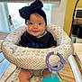 baby, baby_seat, black_bow, child, childhood, cute, face, happy, headband, indoor, infant, legs, natural_light, patterned_fabric, person, plaything, seated, smile, toy, window