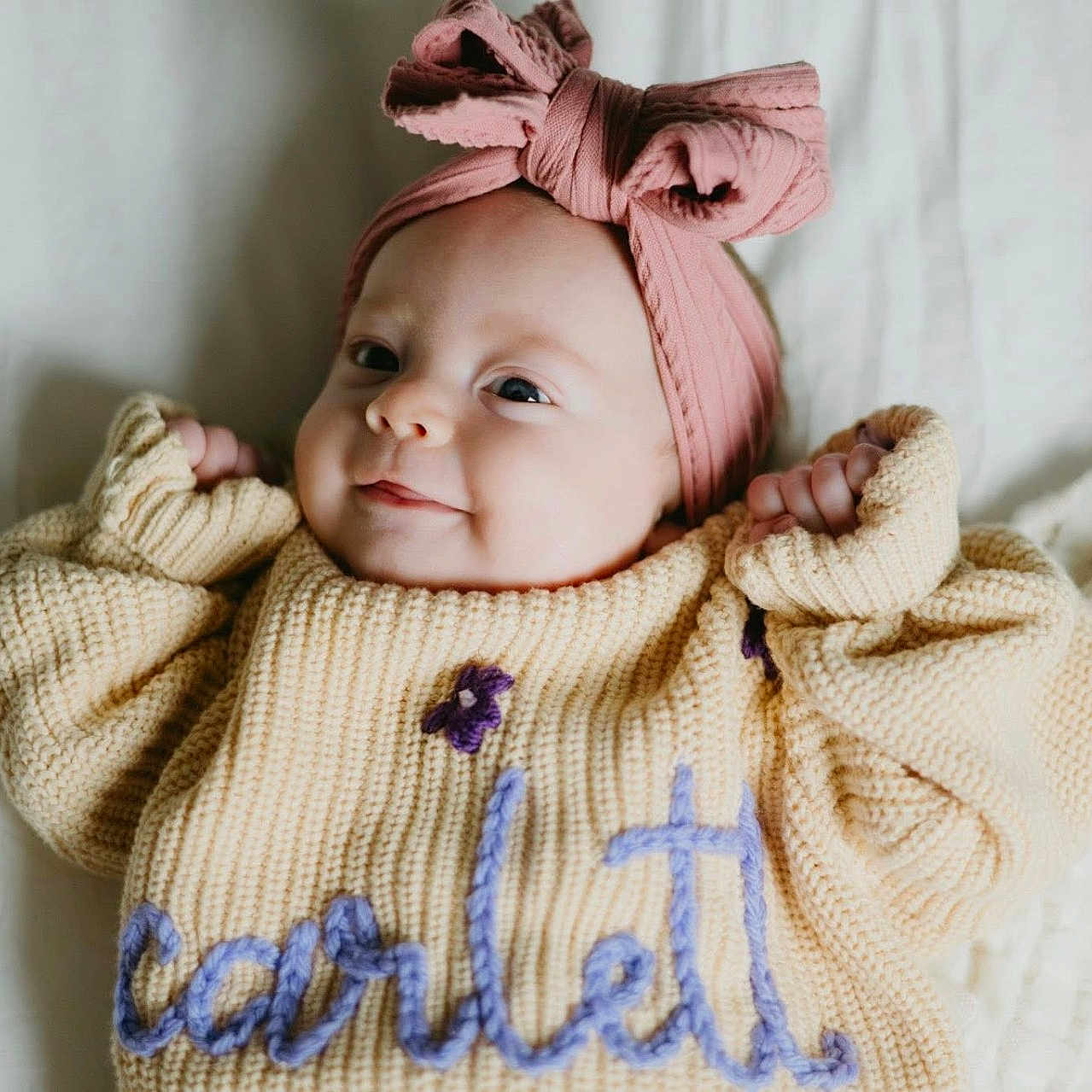 Scarlettt is registered to the contest to win money with this photo: baby, bed, blanket, bow, child, closeup, cozy, cute, face, hands, happy, headband, indoor, infant, knitted_sweater, lying_down, portrait, smiling, soft_light, warm_colors