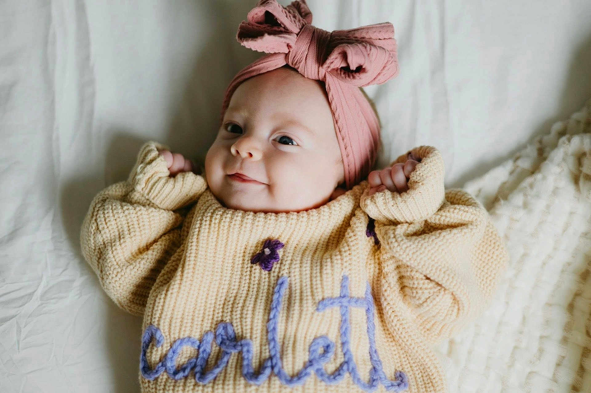 Scarlettt is registered to the contest to win money with this photo: baby, bed, blanket, bow, child, closeup, cozy, cute, face, hands, happy, headband, indoor, infant, knitted_sweater, lying_down, portrait, smiling, soft_light, warm_colors